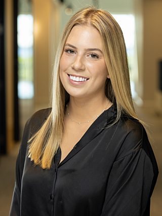 Smiling professional woman with blonde hair wearing a black blouse in a modern office hallway.