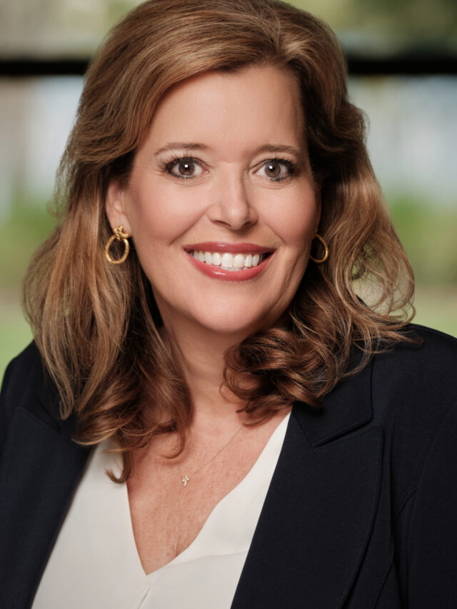 Professional headshot of a smiling woman in a dark blazer against a softly blurred background.