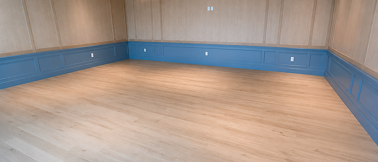 ADA-compliant multipurpose gathering room featuring light wood flooring, decorative blue wainscoting, paneled wood walls, and brass chandelier lighting.