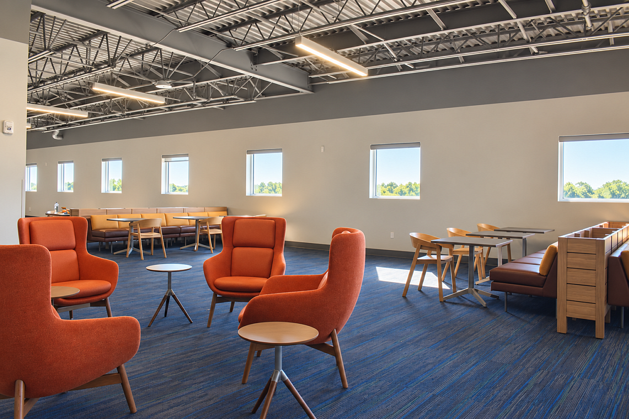 Library lounge with rust-orange armchairs, brown upholstered booths, wood tables, and blue carpeting.