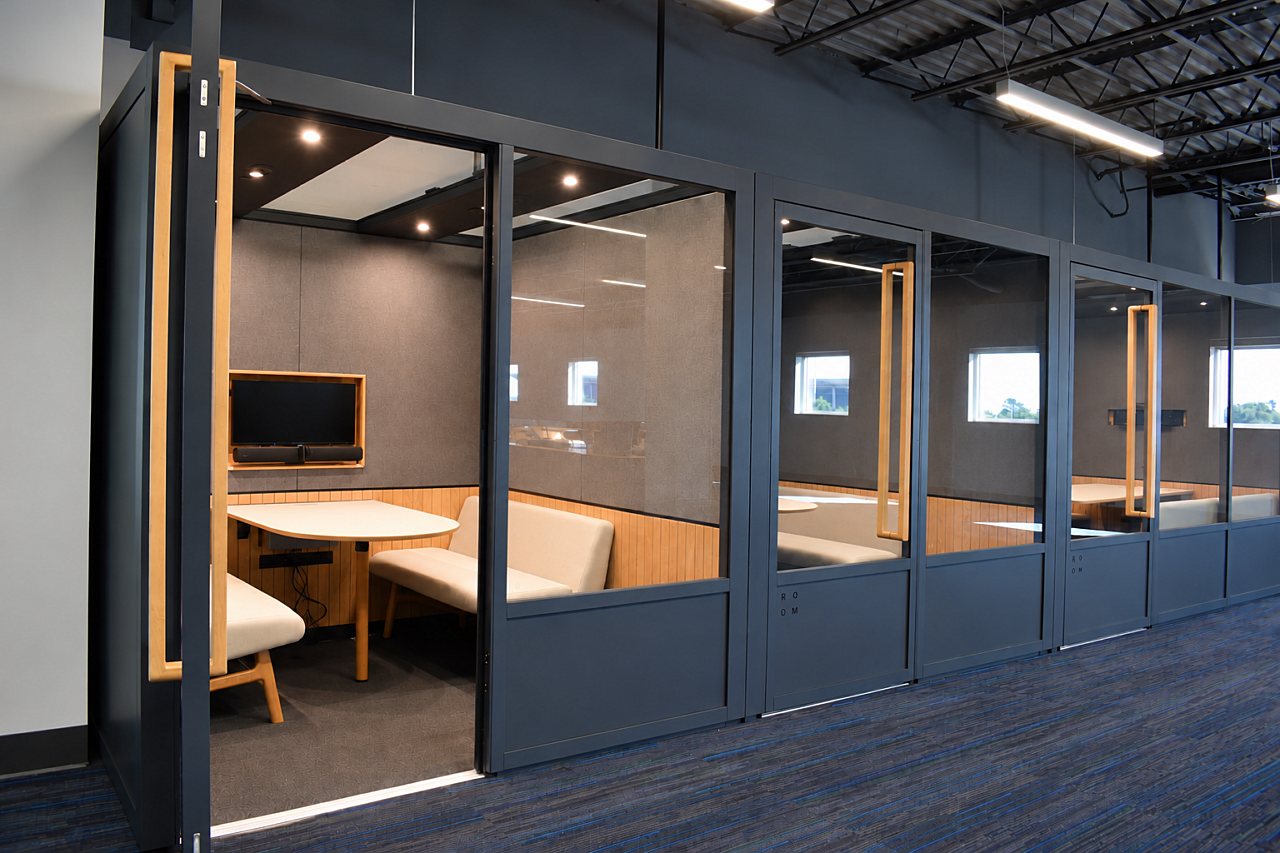 Glass-enclosed library study pods with private seating, tables, and integrated screens.