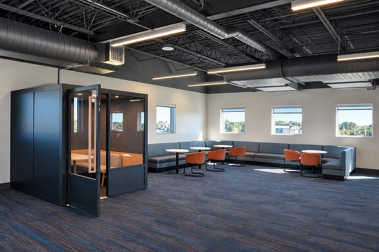 Library lounge with a private study pod, gray sectional seating, orange chairs, and blue carpeting.