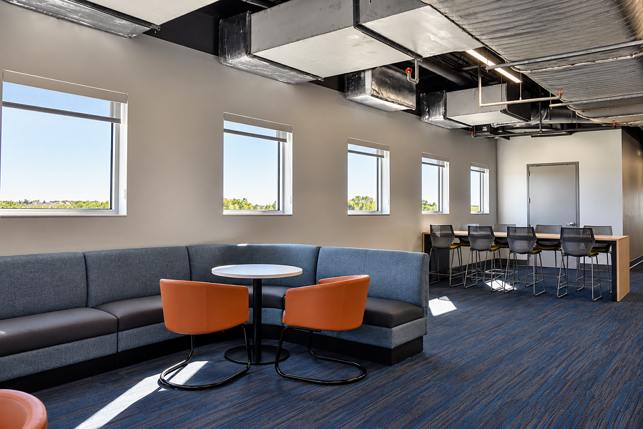 Library lounge with curved blue seating, orange chairs, round tables, and a high-top study area.