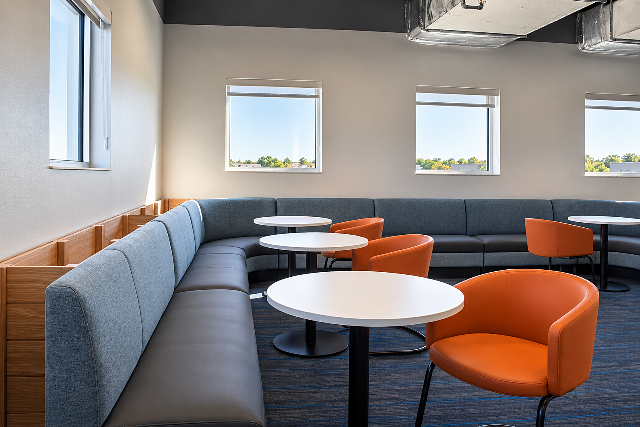 Library lounge with blue banquette seating, orange chairs, round tables, and natural light from windows.