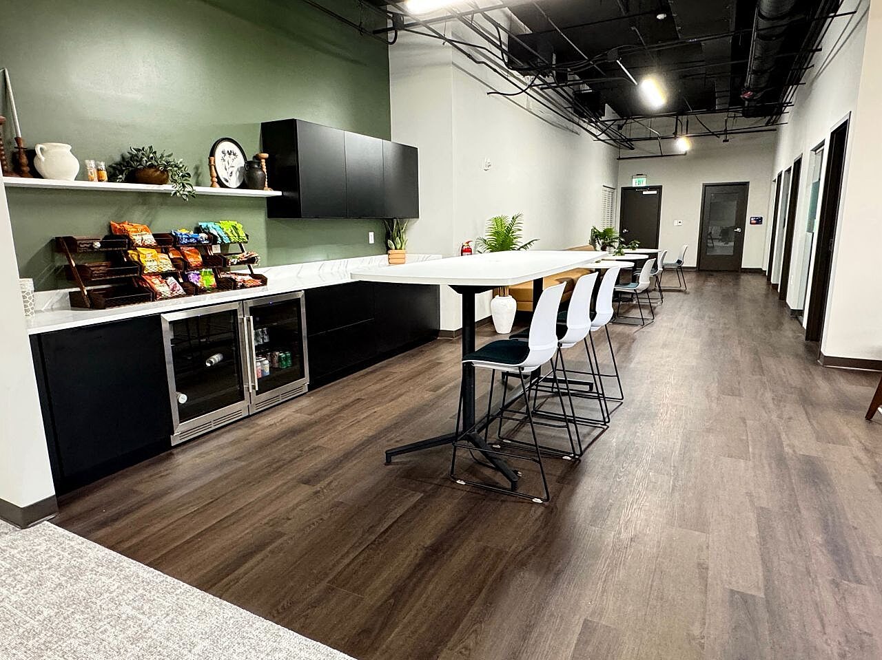 Modern office café with bar-height seating, black cabinetry, snack station and green accent wall.