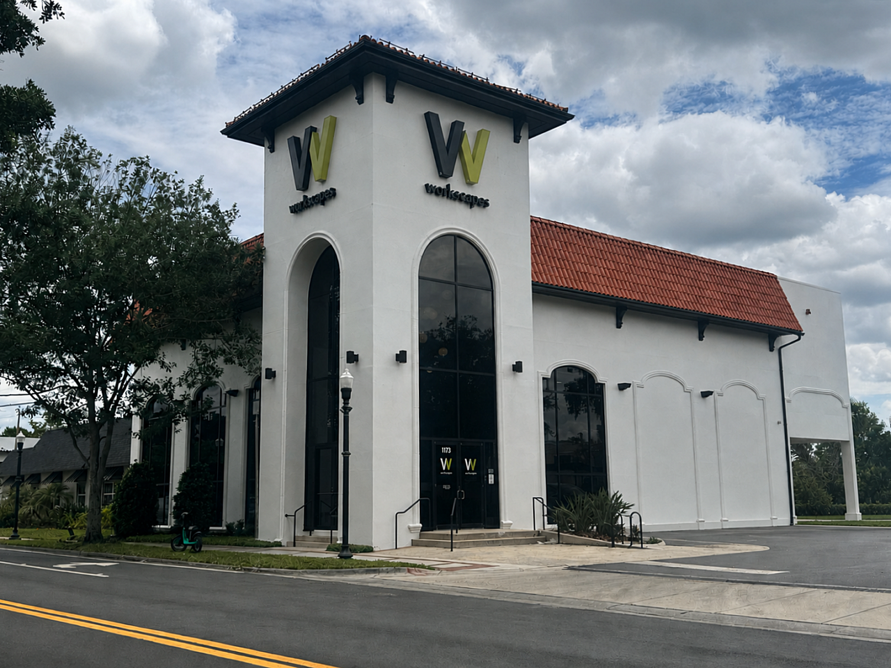 Exterior view of the Workscapes showroom building with white stucco walls, red tile roof, and branded tower entrance.