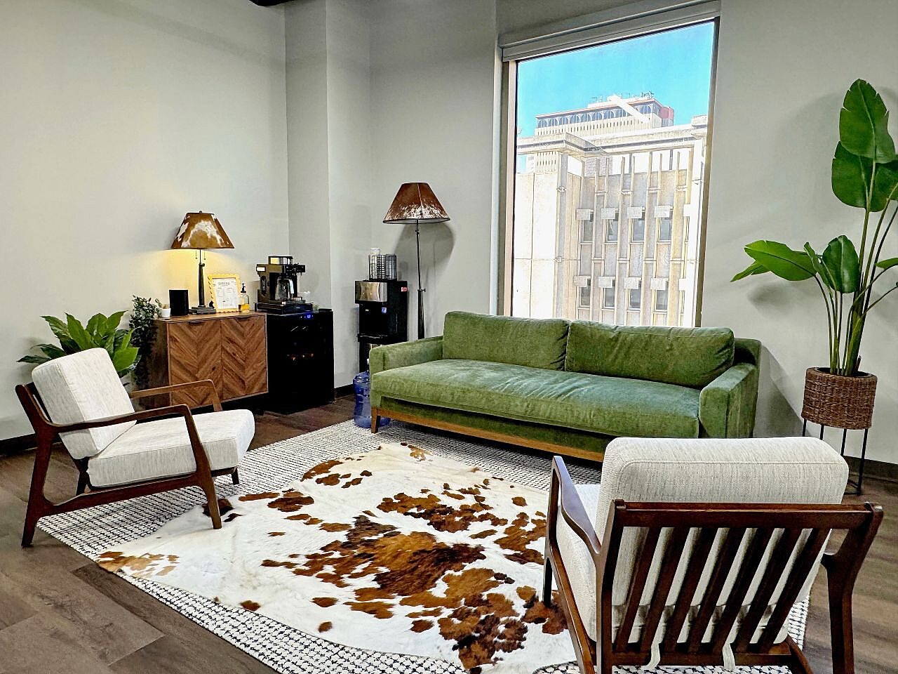 Comfortable office lounge with a green sofa, upholstered chairs, layered rugs and large windows.