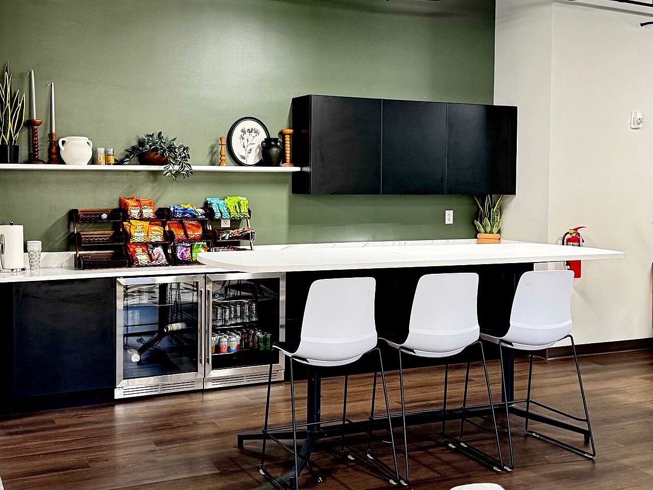 Office café and break area with bar-height seating, black cabinetry, refreshments and green accent wall.