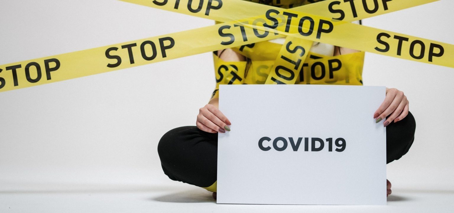 Person wrapped in caution tape with sign that says COVID-19