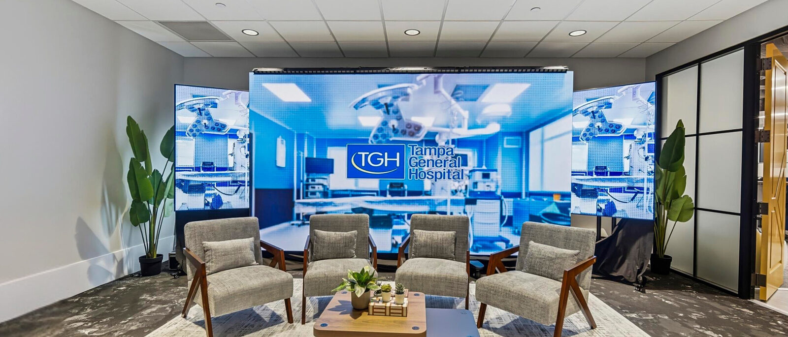 Meeting space with lounge chairs facing digital display showing Tampa General Hospital branding.