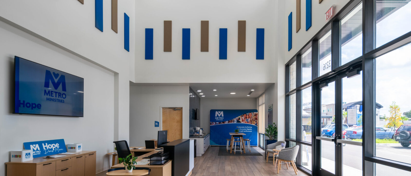 Modern lobby with wood floors, tall ceilings, and Metro-branded welcome desk near large windows.