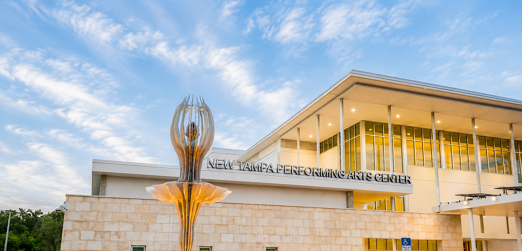 Exterior view of the New Tampa Performing Arts Center with sculpture and dramatic sky backdrop.
