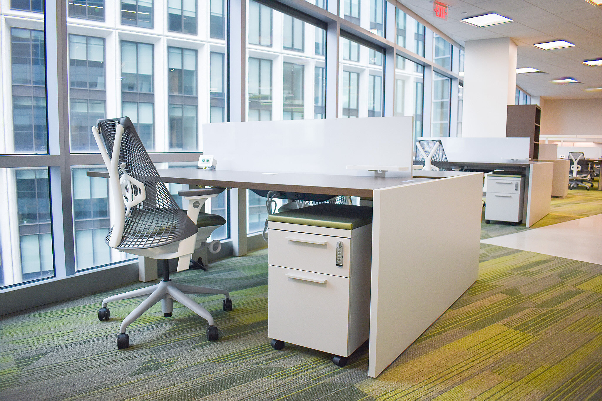 Private workstation with ergonomic chair, mobile pedestal, and floor-to-ceiling windows.