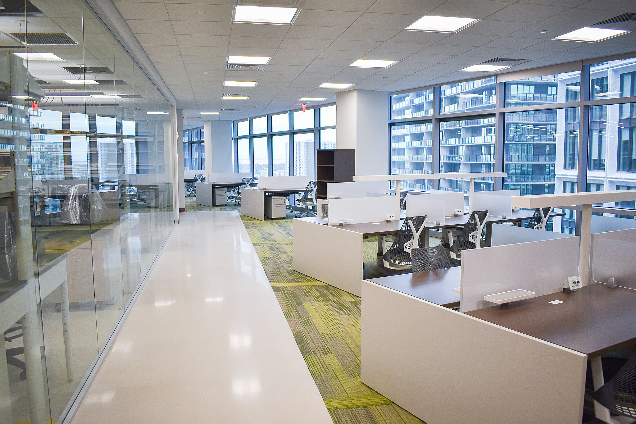 Open office with benching workstations, glass conference rooms, and city views through large windows.