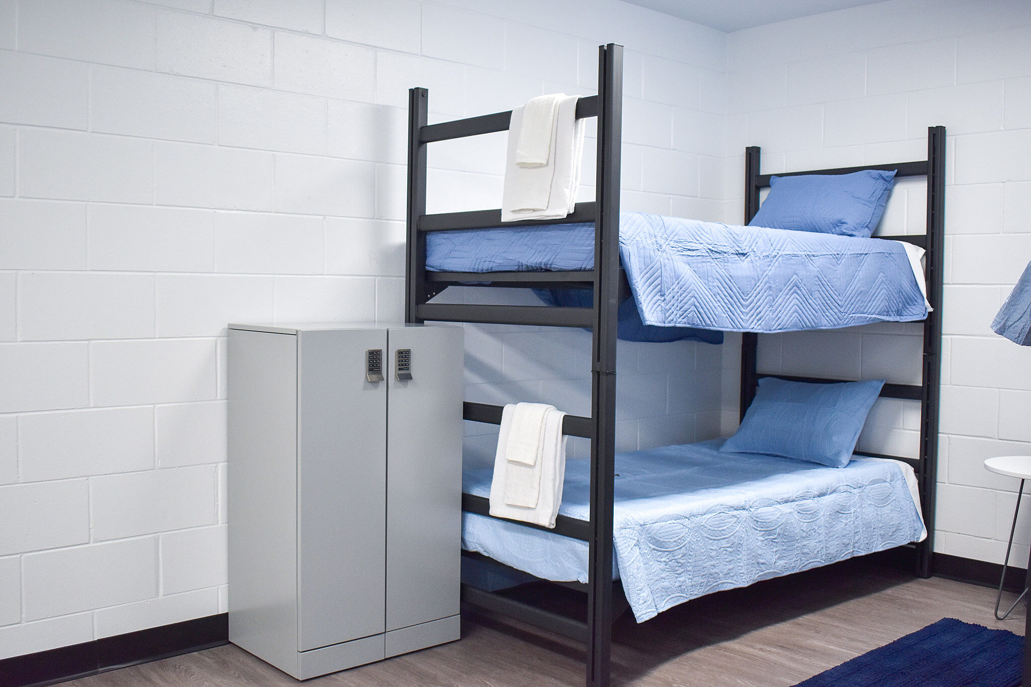 Bunk beds with blue bedding beside a small gray metal locker in a simple dorm-style room.
