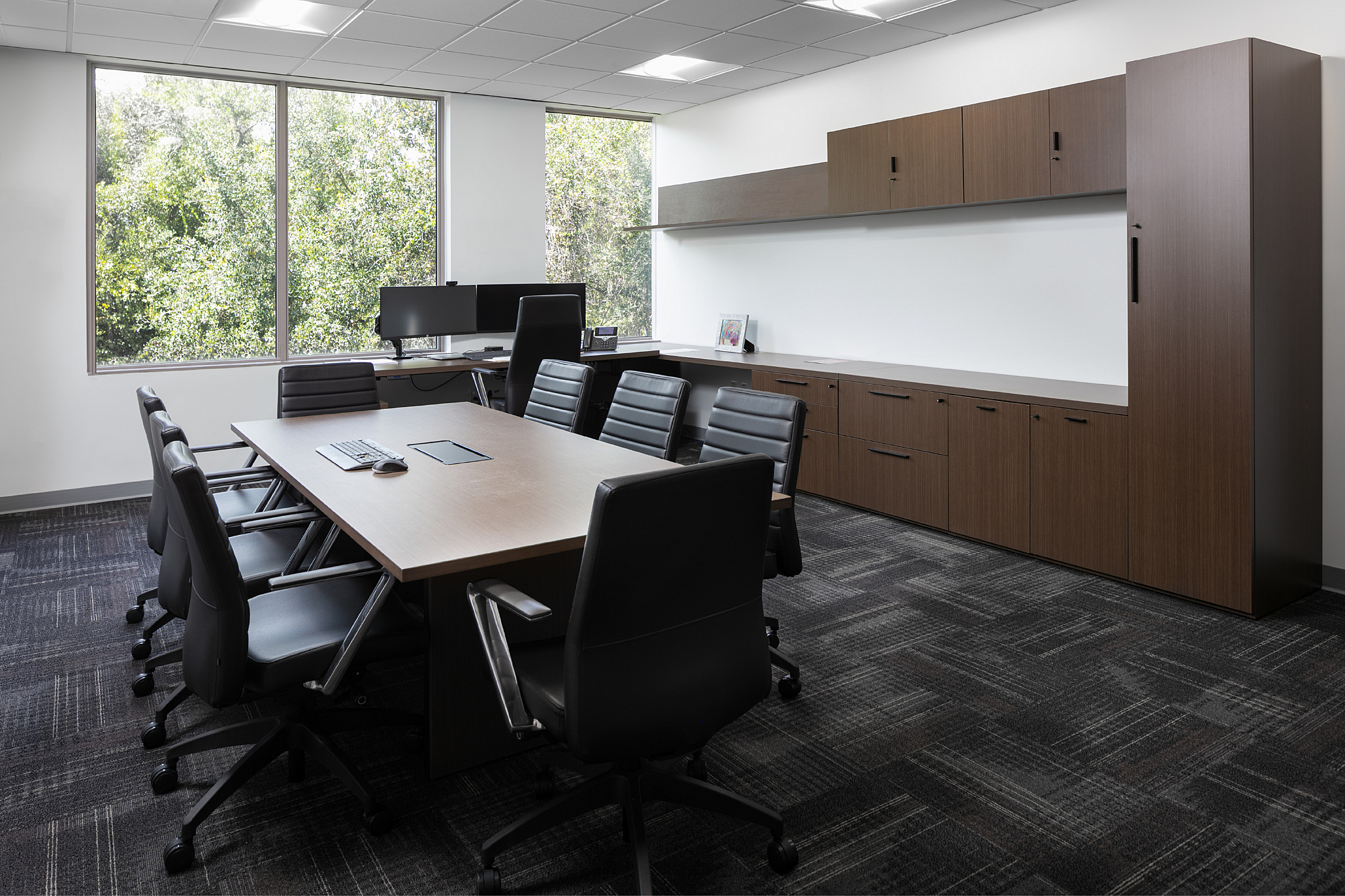 Private office with a large meeting table, wood storage, workstation and expansive windows.