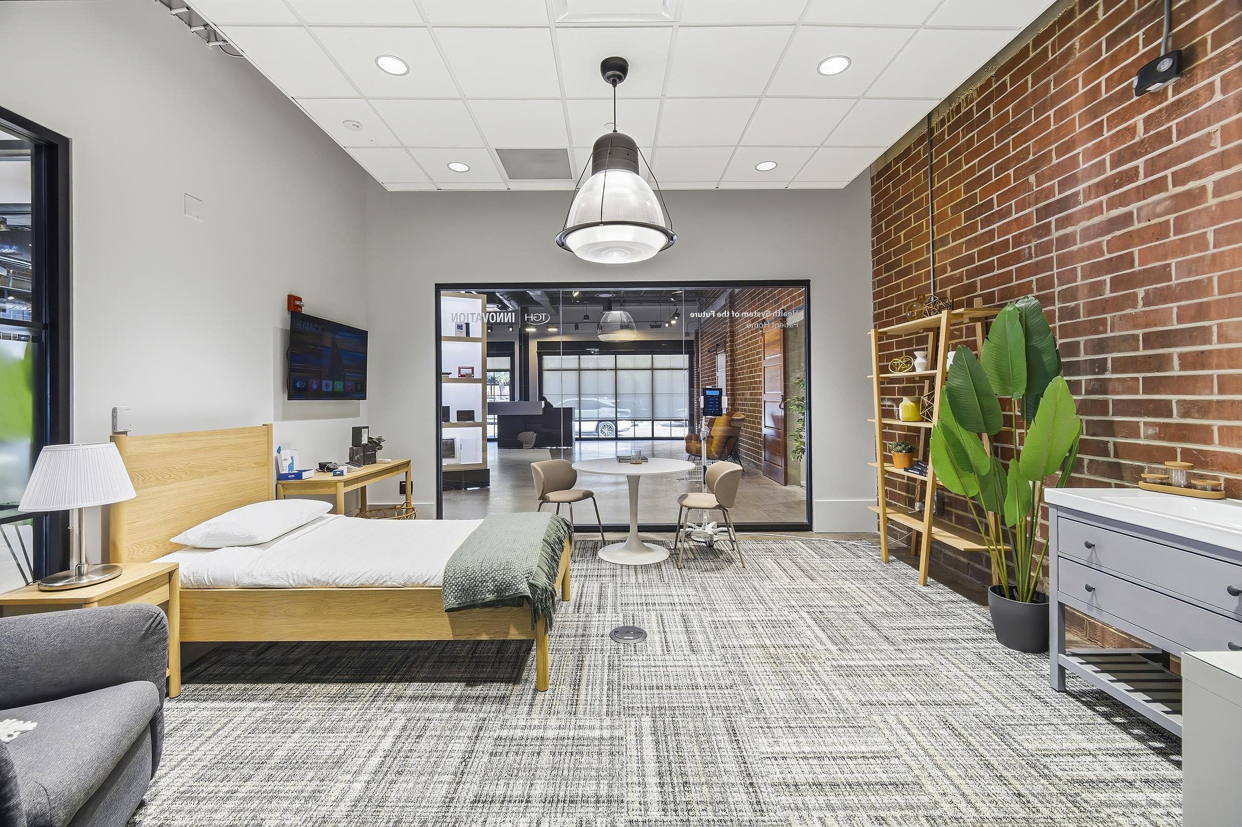 Mock residential room with bed, side table, shelving, and exposed brick accent wall.