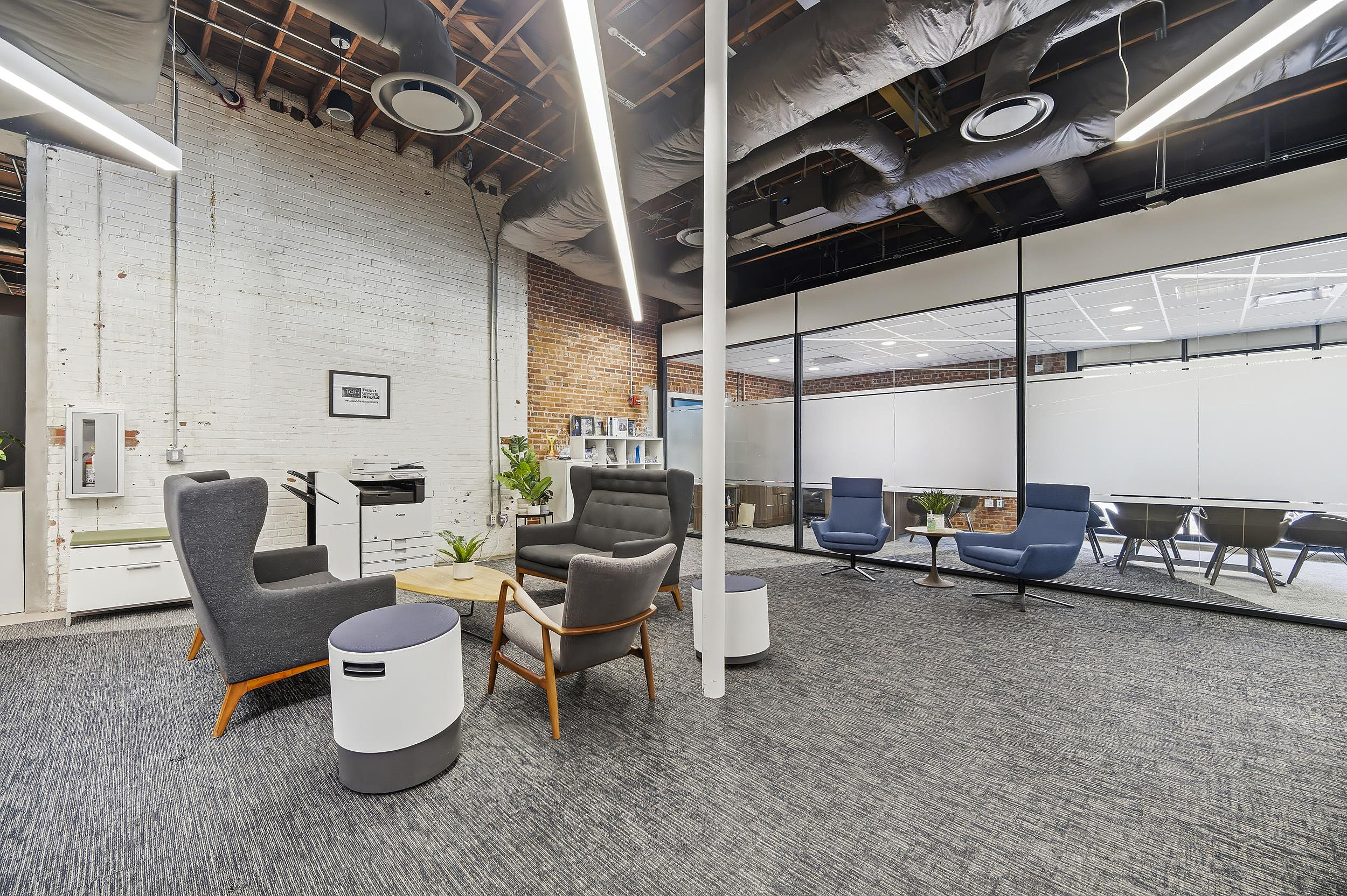 Collaborative office lounge with upholstered chairs, coffee table, and glass-walled meeting room.