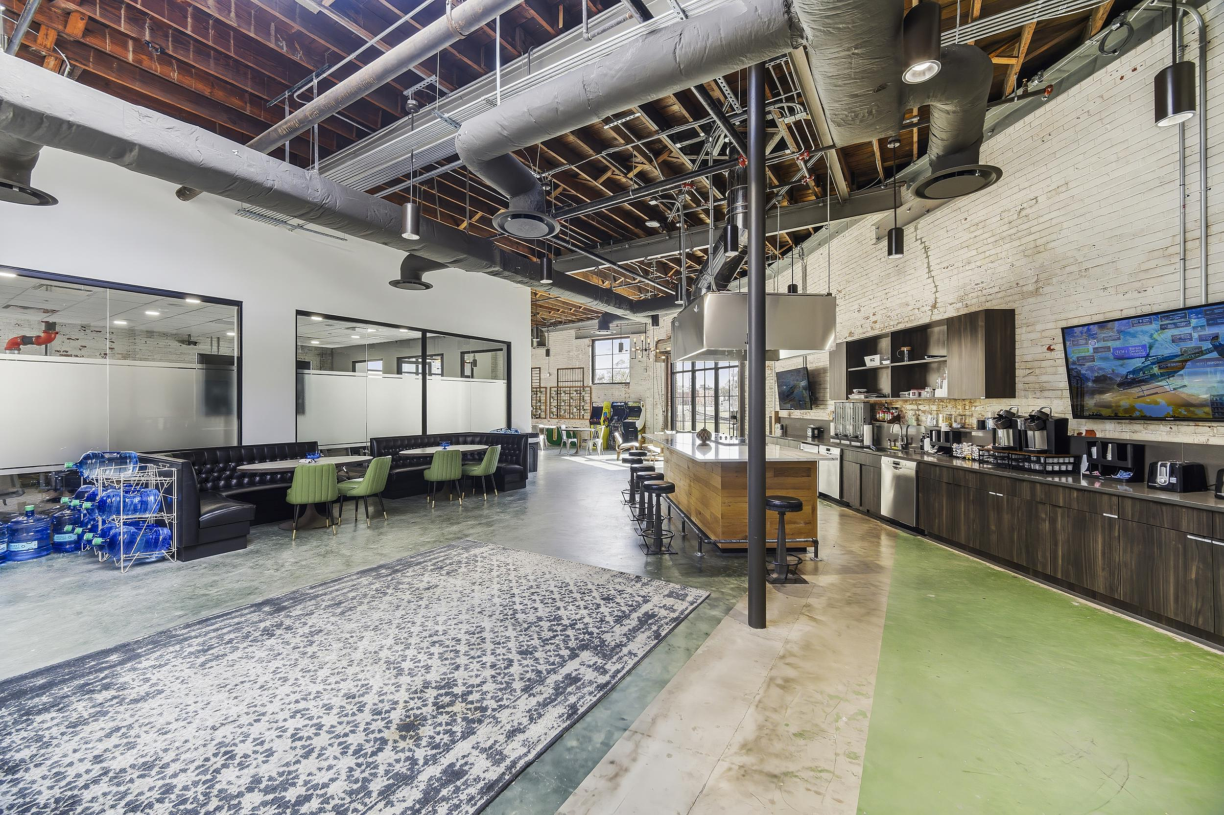 Industrial-style breakroom with bar seating, lounge booths, and exposed ceiling ducts.