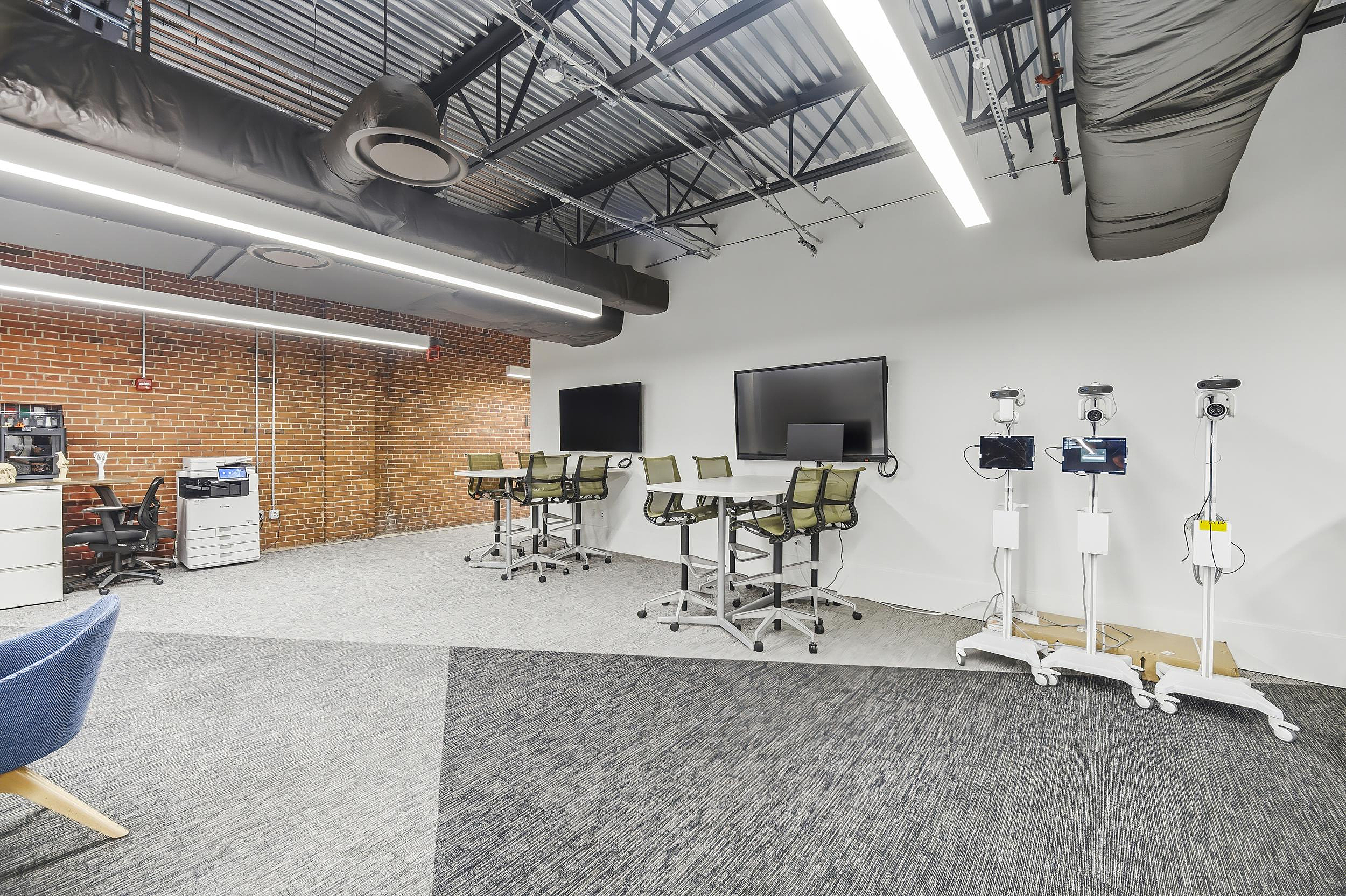 Innovation lab with standing tables, monitors, and telepresence robots in open workspace.