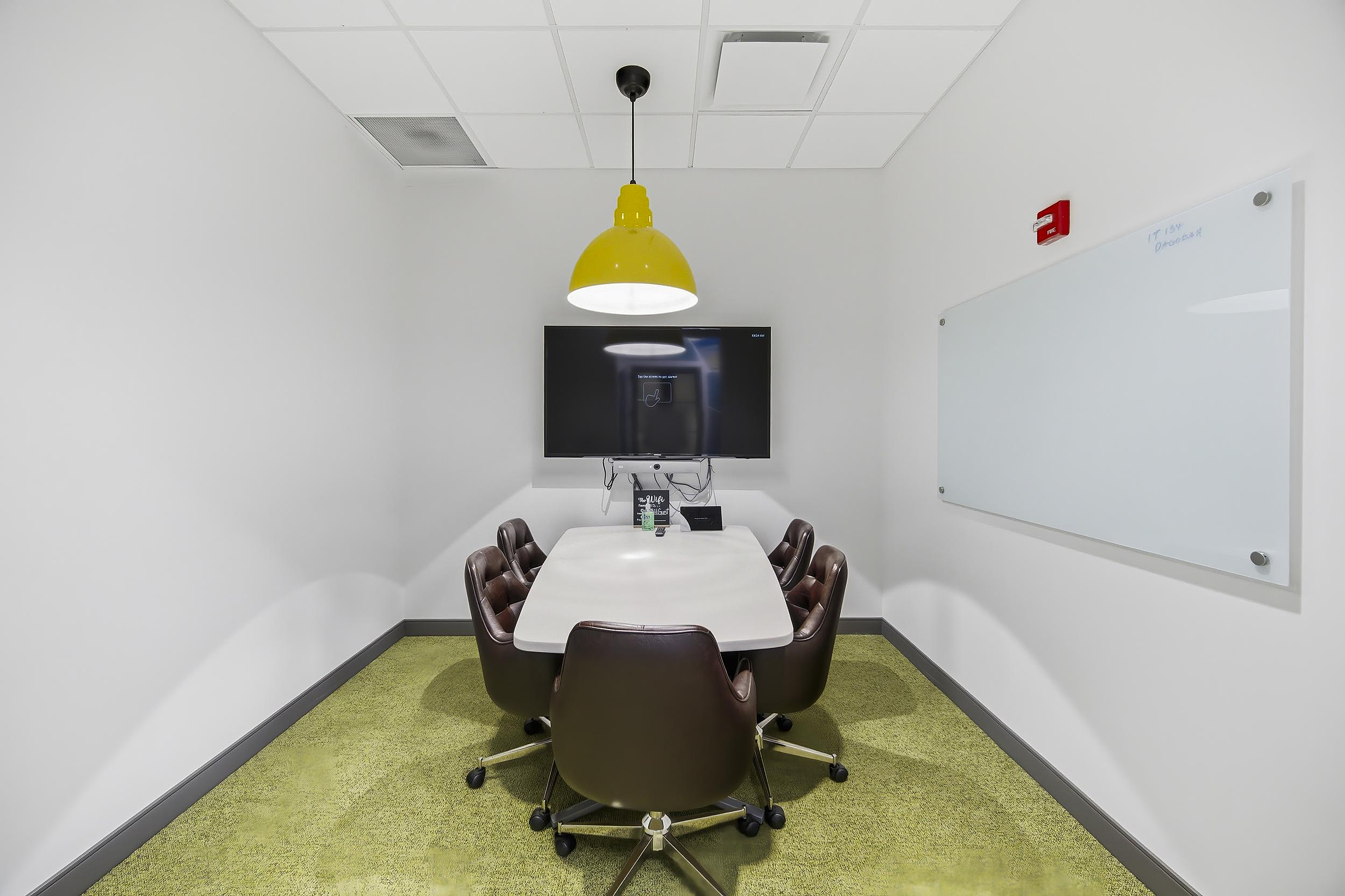 Small meeting room with conference table, brown chairs, wall display, and whiteboard.