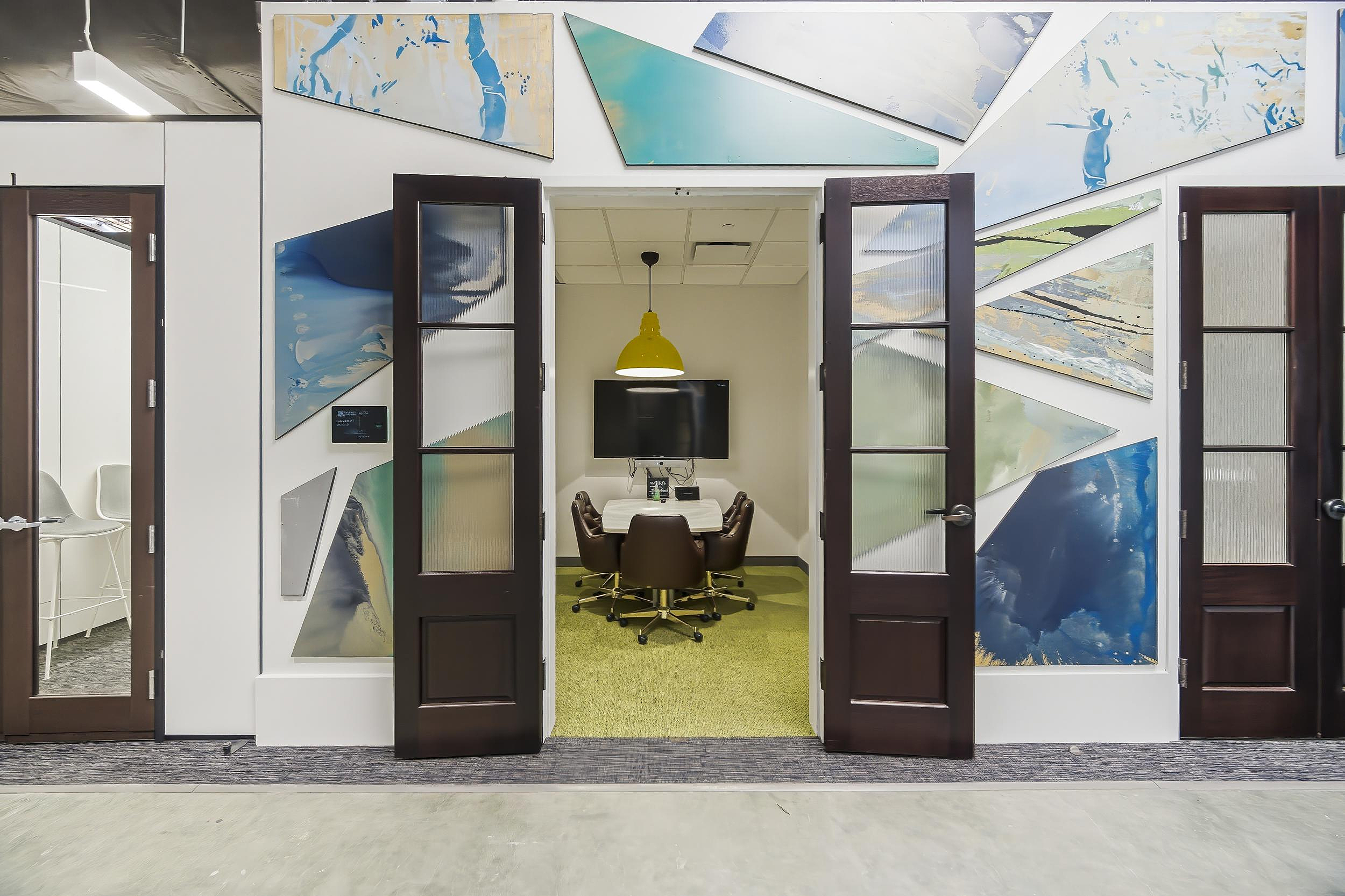 Meeting room with round table, wall display, and abstract geometric mural at entrance.