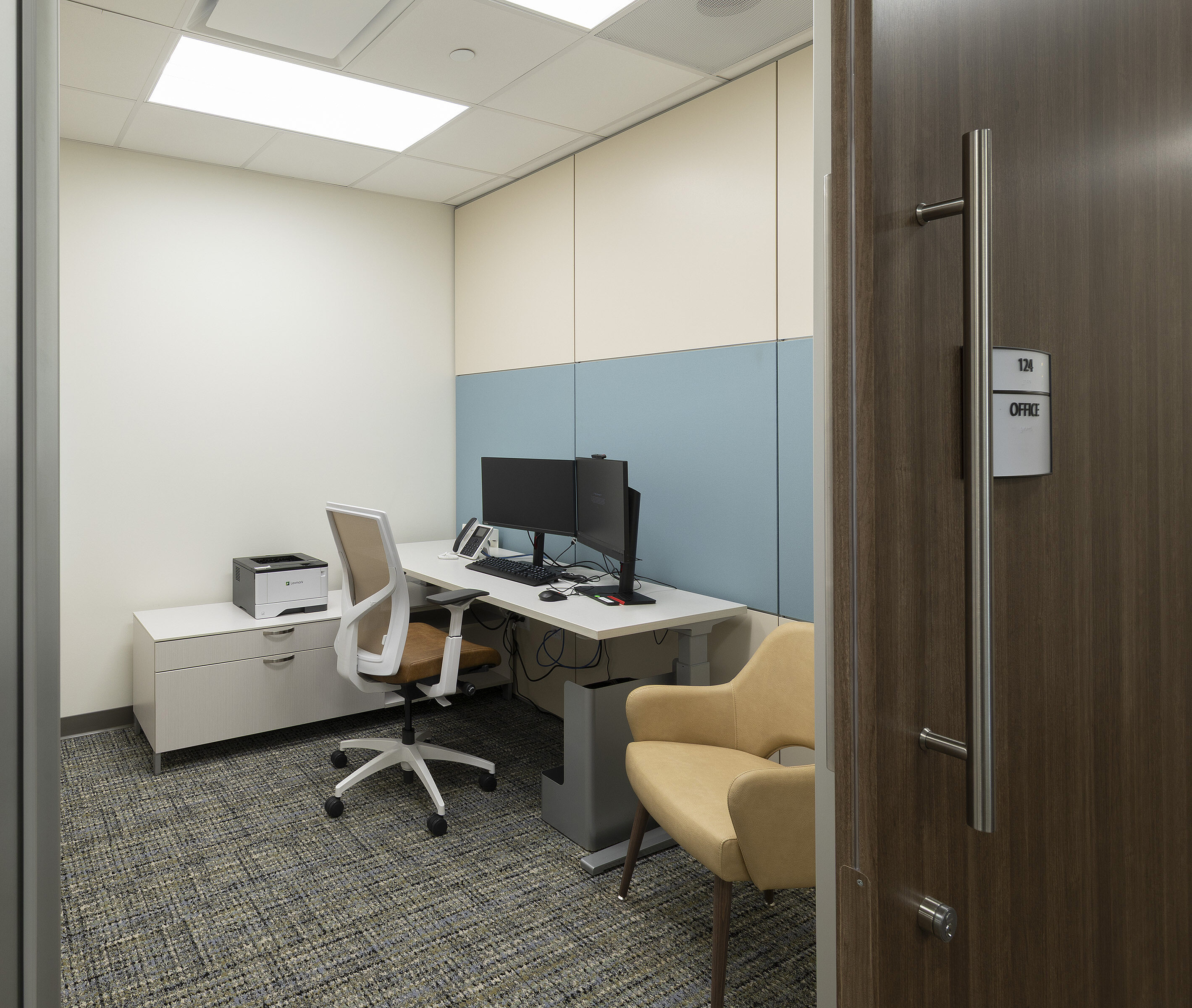 Small office with desk, dual monitors, white chair, printer, and a yellow guest chair.