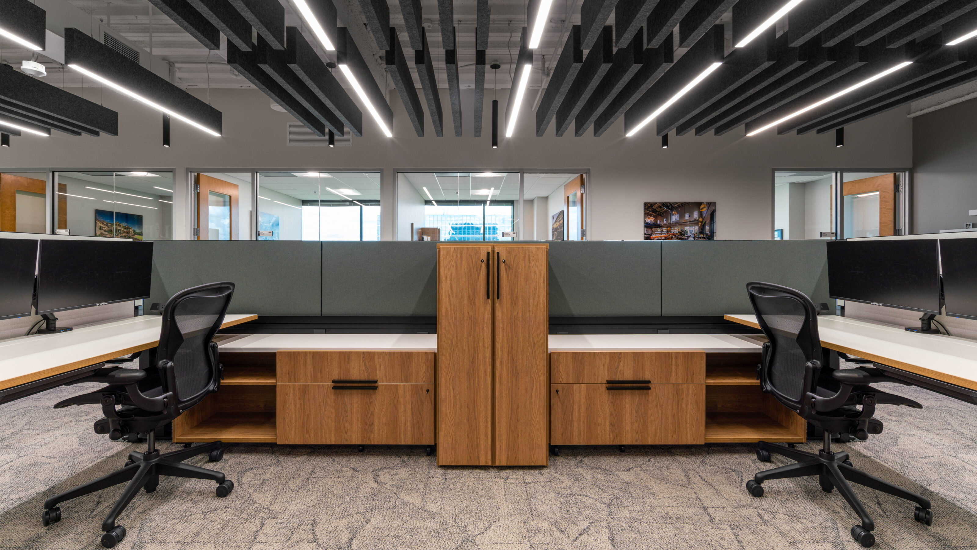 Dual workstations with wood storage, mesh chairs, and overhead acoustic panels in a modern office.