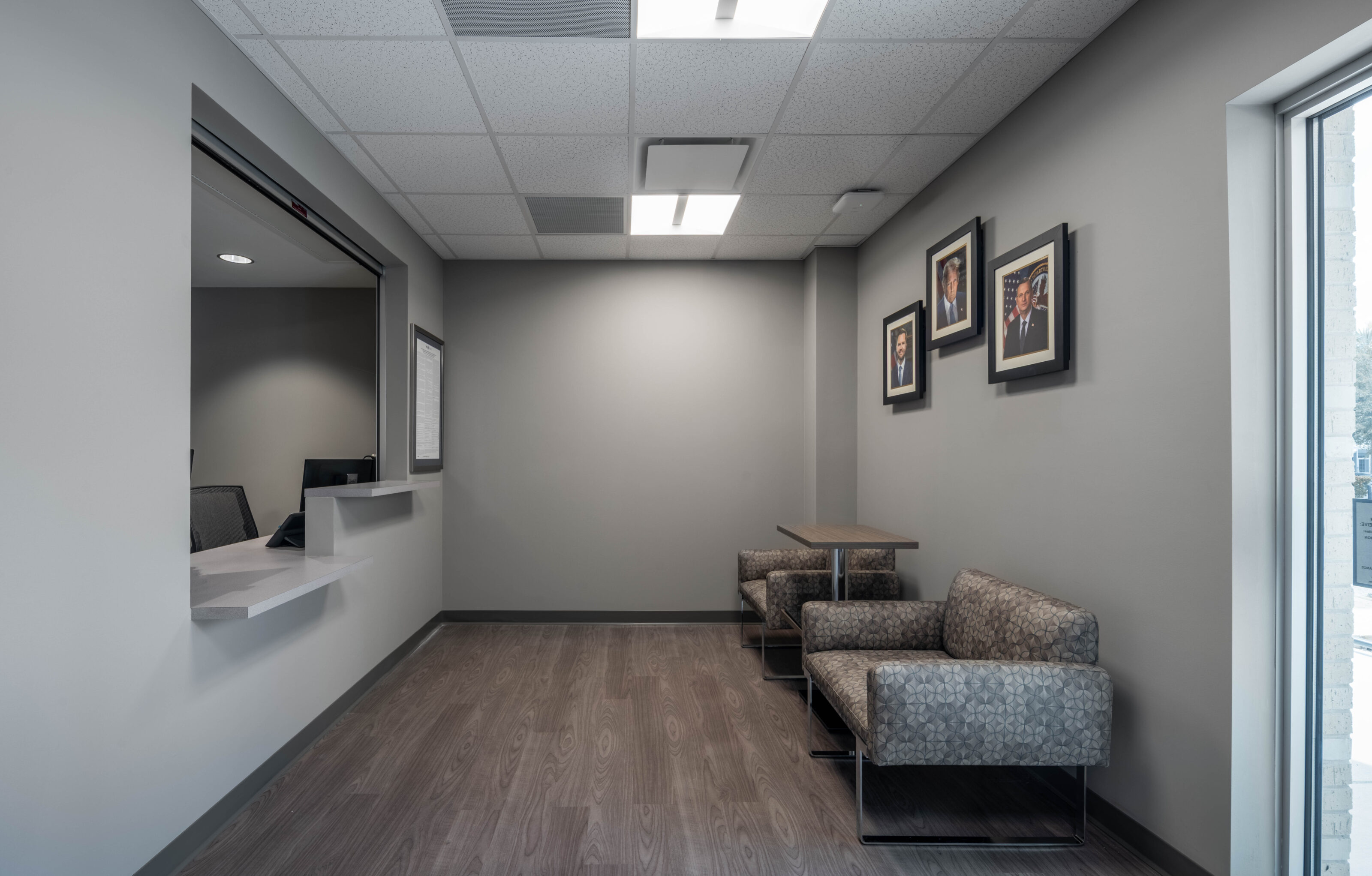 Small waiting area with patterned chairs, a reception window, and framed artwork on gray walls.
