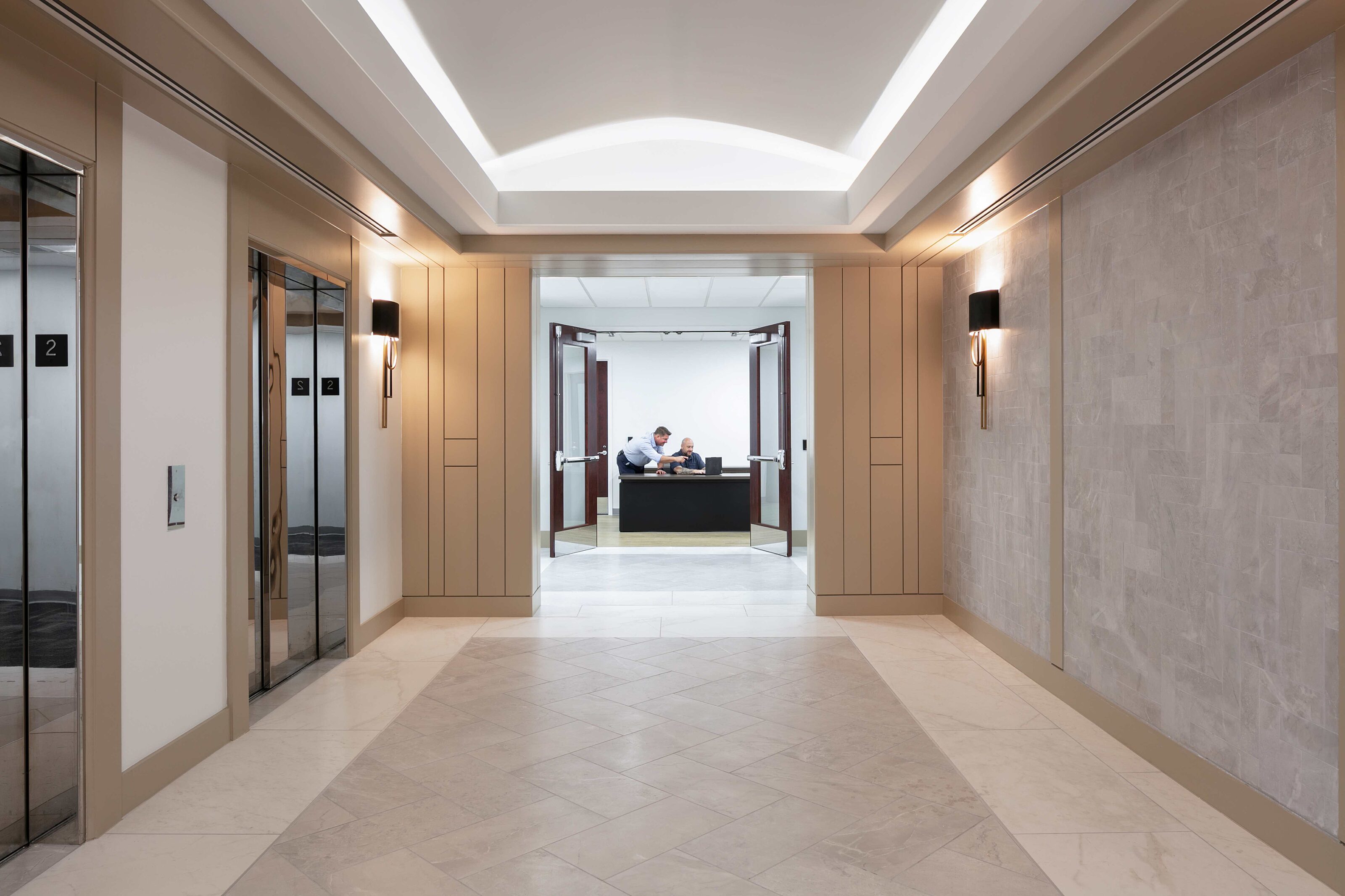 Modern elevator lobby leading to an office reception area where two employees collaborate.