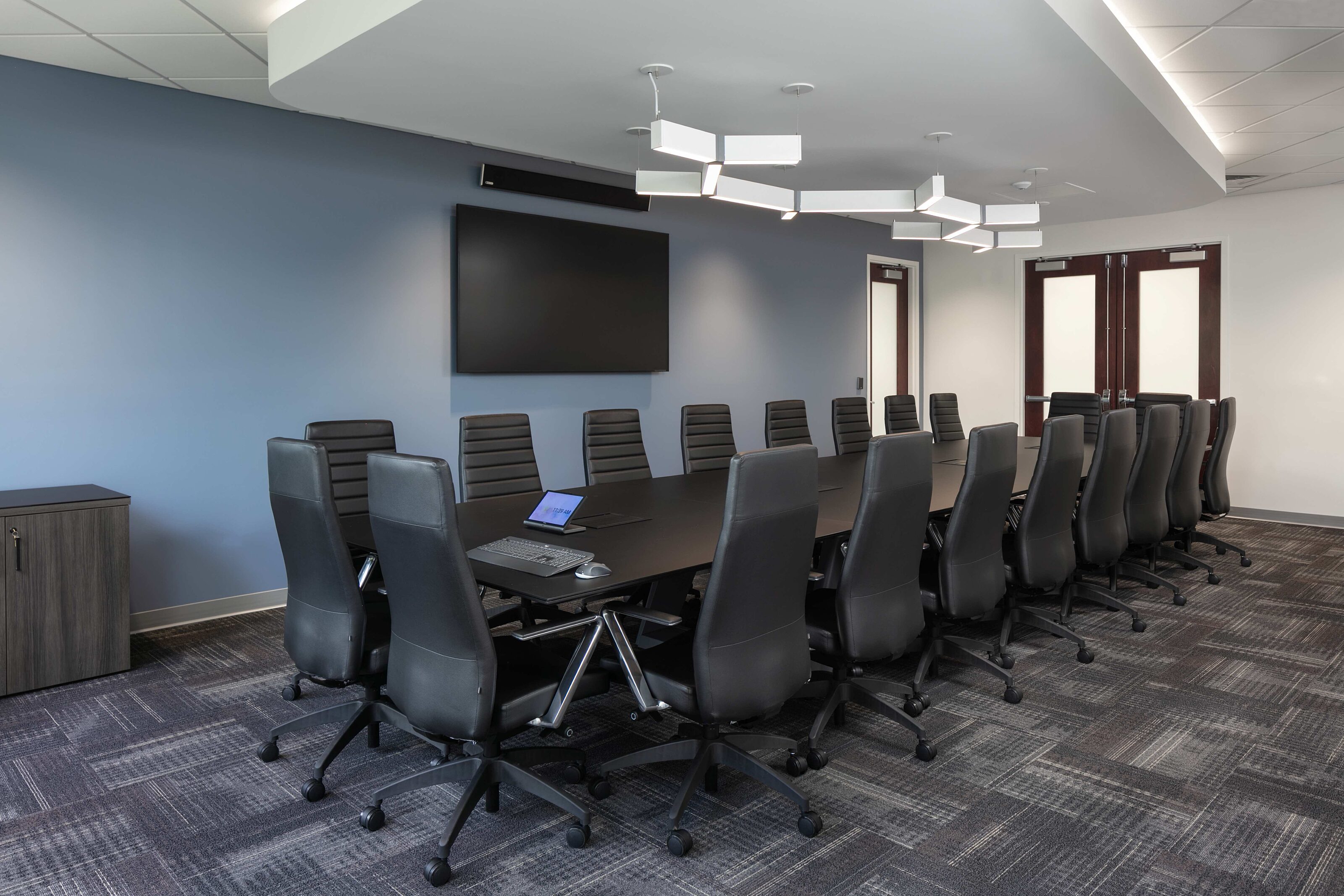 Large conference room with a long table, black chairs, wall display and modern lighting.