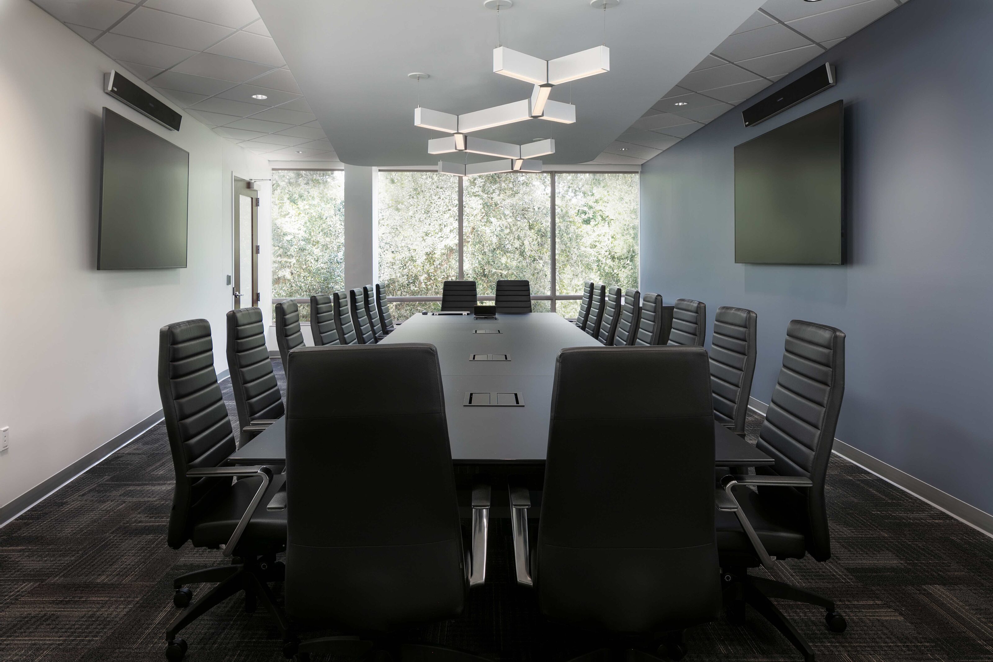 Large conference room with a long table, black chairs, dual displays and floor-to-ceiling windows.