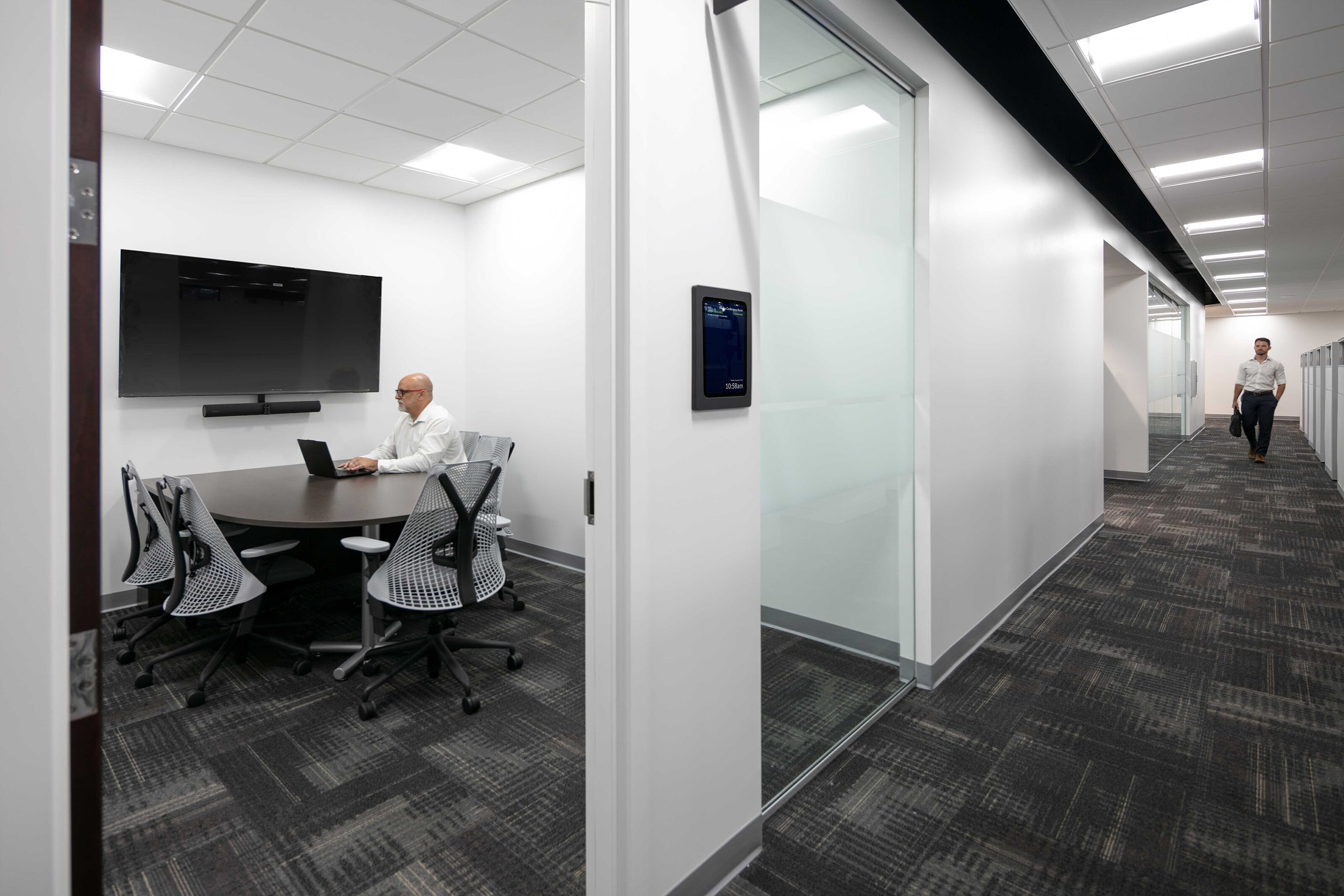 Modern office corridor with a glass conference room, collaborative seating and employees working.