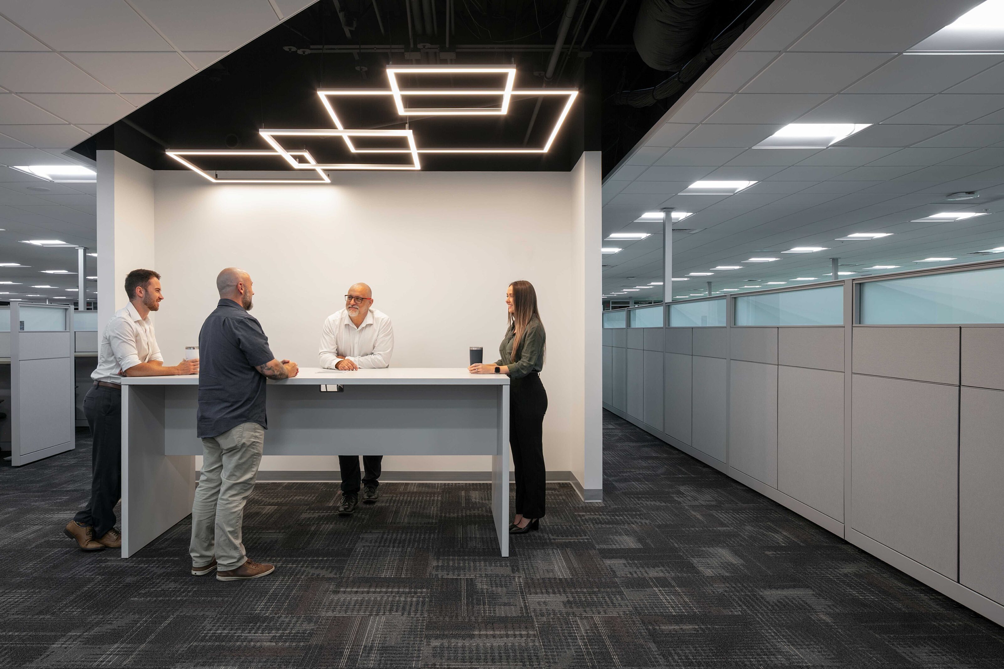 Four employees gather around a standing-height table in a modern open office.