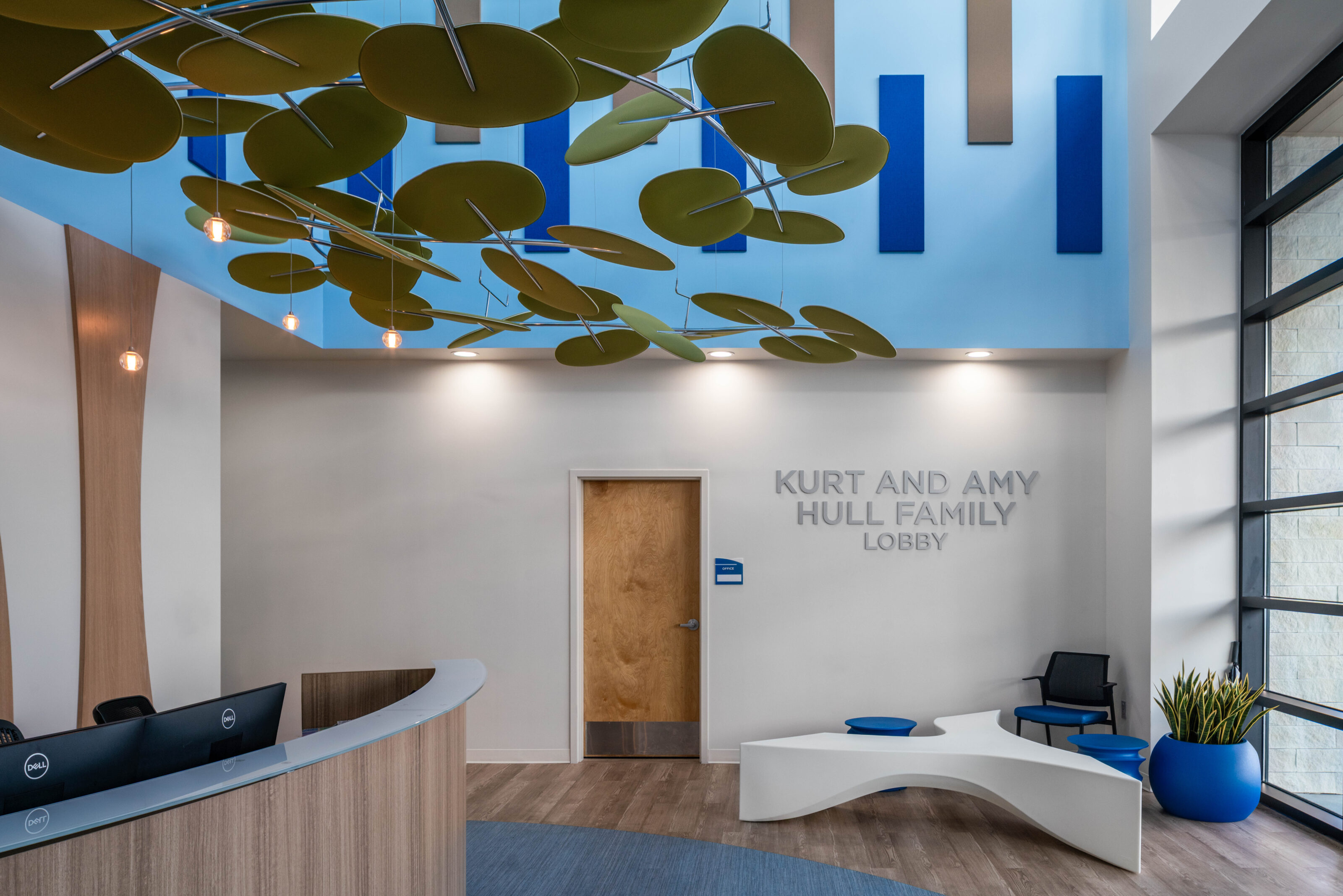 Modern lobby with leaf ceiling art, curved seating, blue accents, and wall sign for Mull Family Lobby.