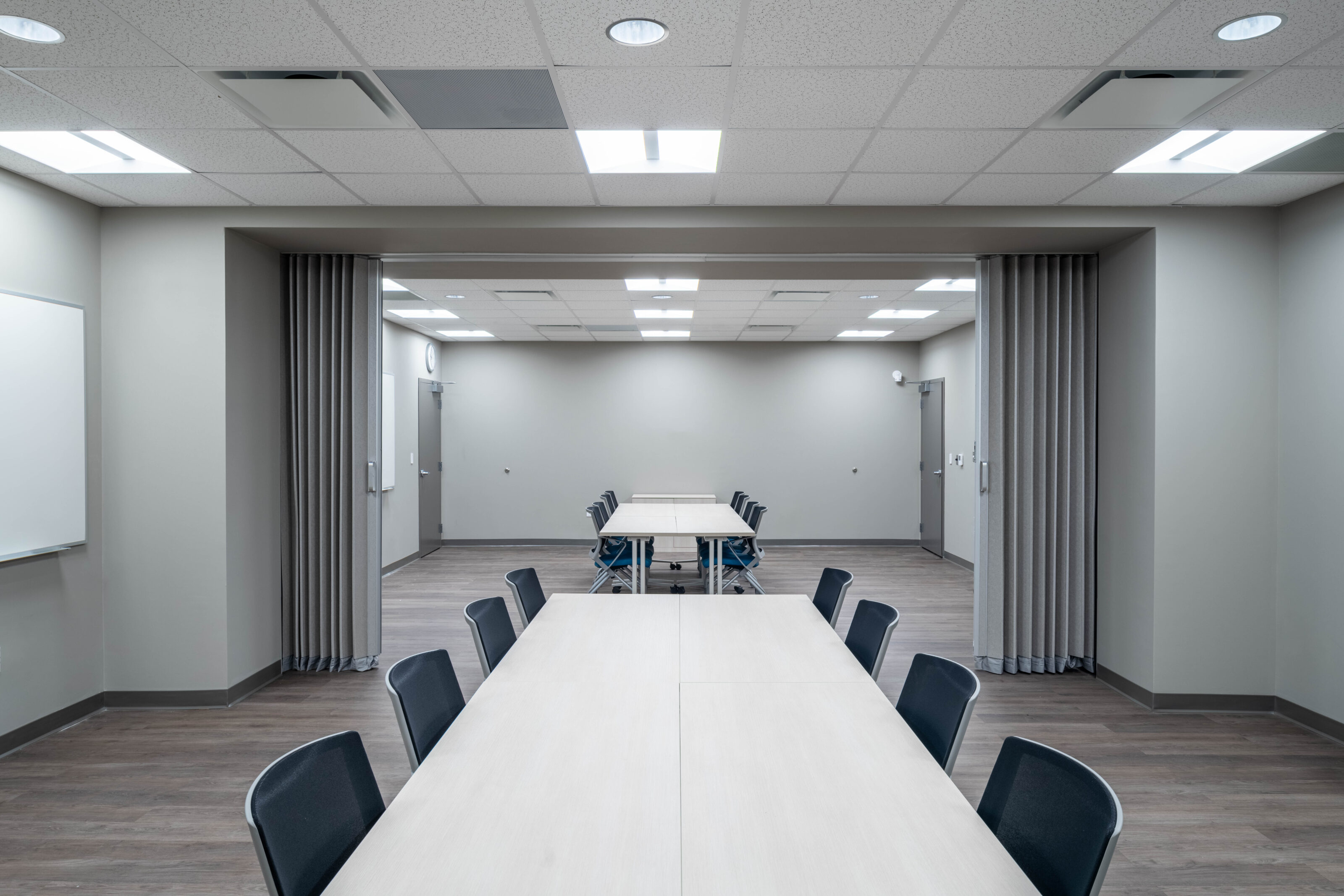 Meeting room with long tables, chairs, and a person pulling a gray partition curtain.