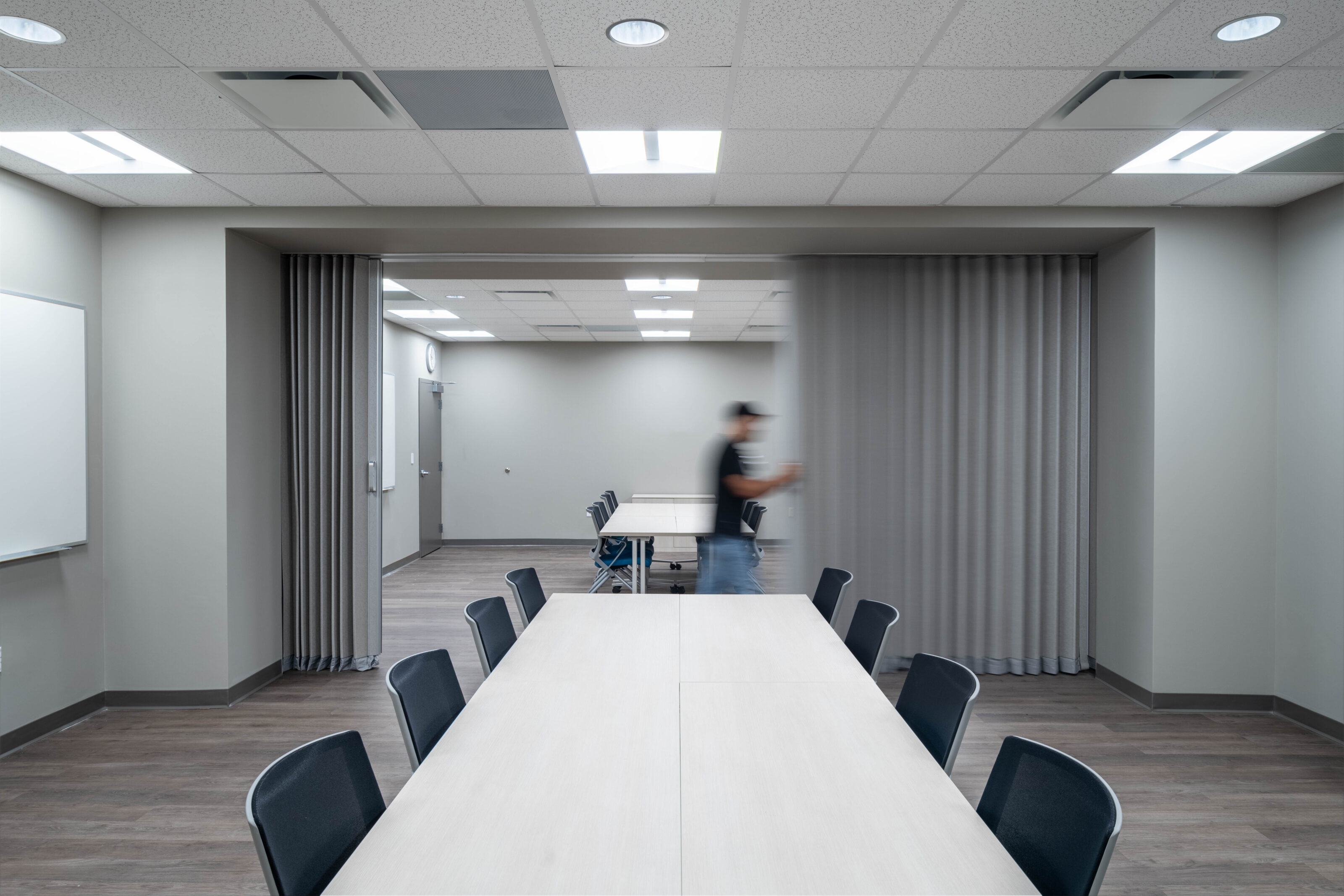 Meeting room with long tables, chairs, and a person pulling a gray partition curtain.
