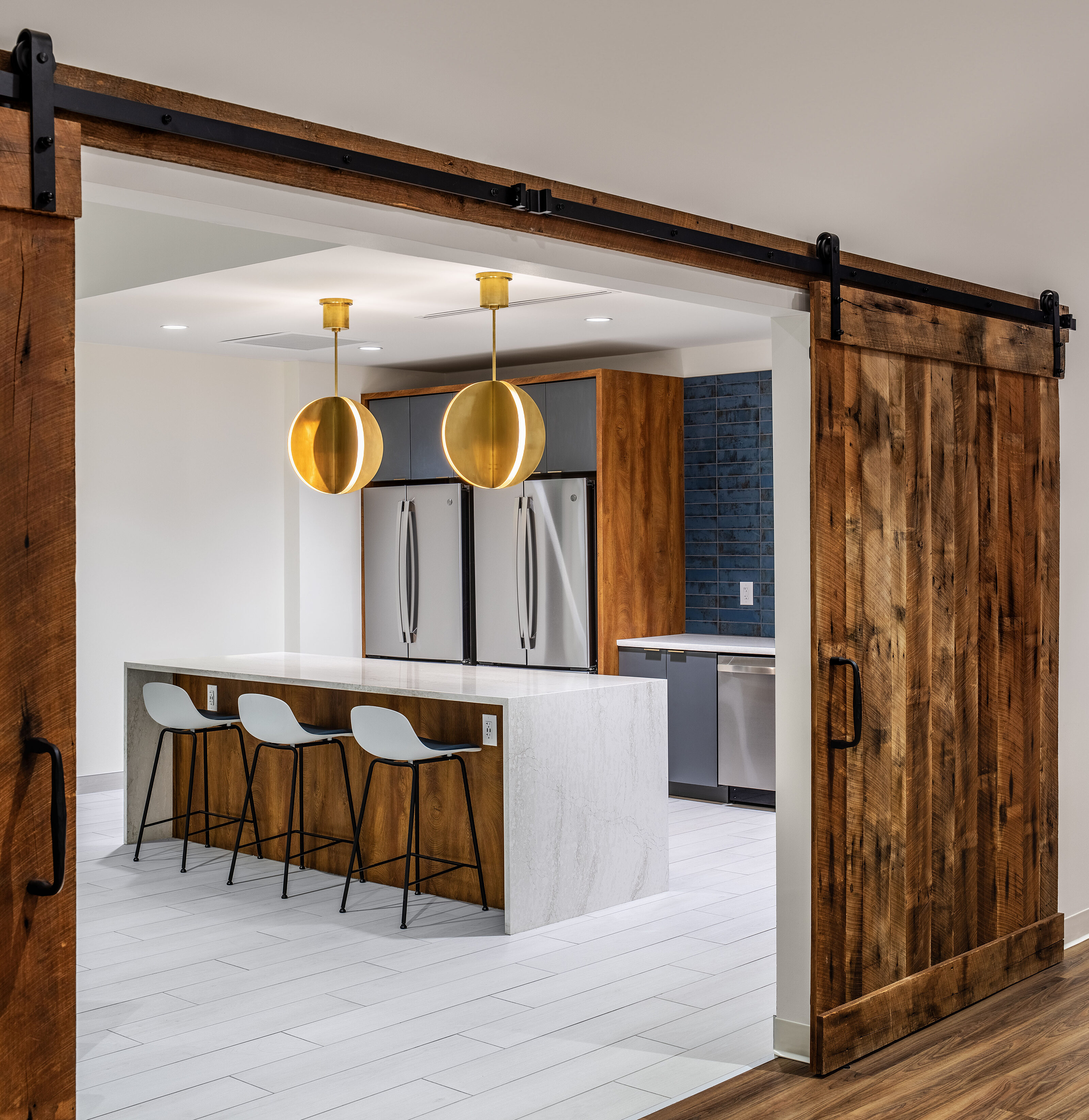 Kitchen with wood barn doors, marble island, gold pendant lights, and stainless appliances.