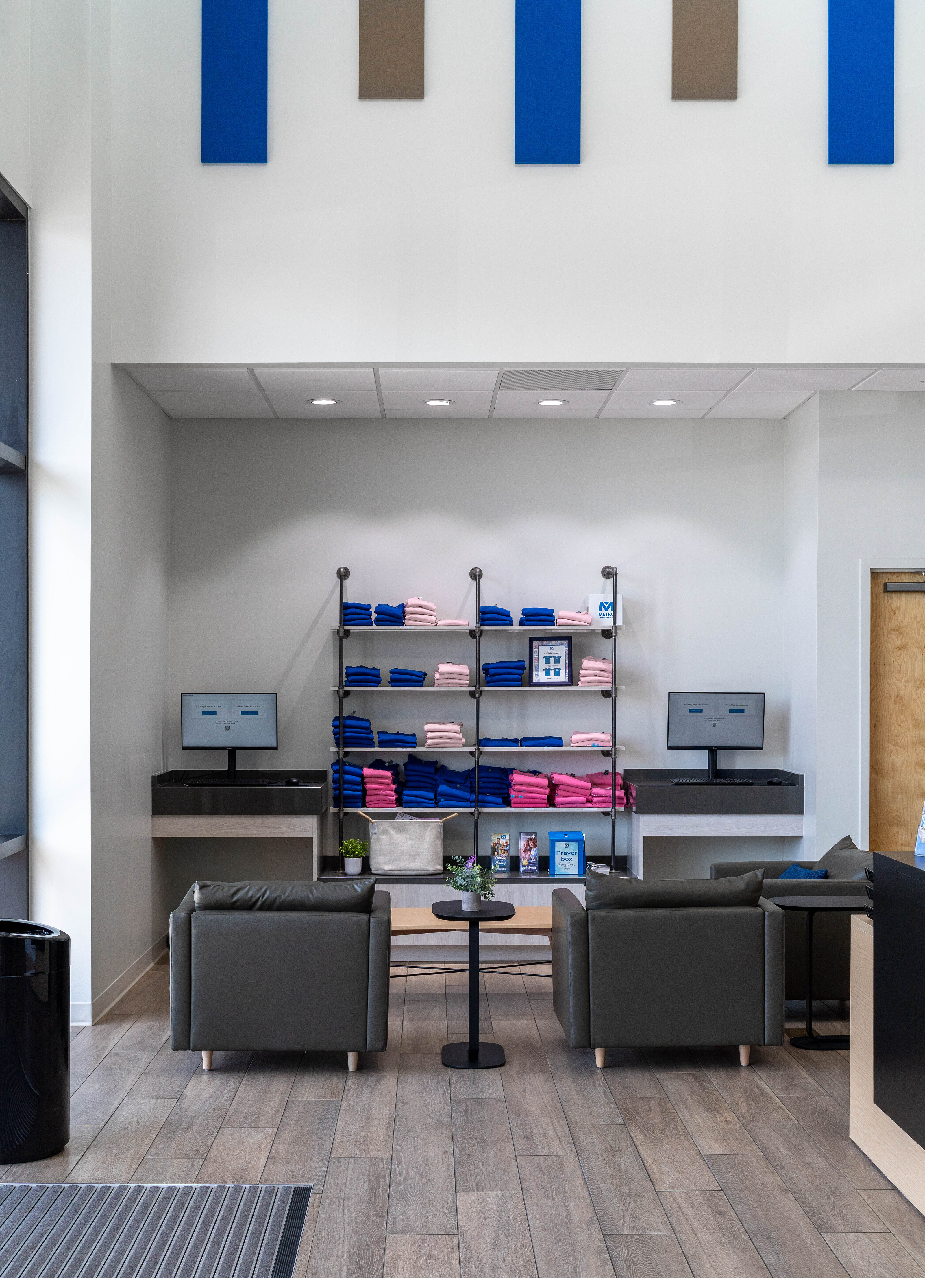 Lobby area with two workstations, gray lounge chairs, shelving with supplies, and tall blue accents.
