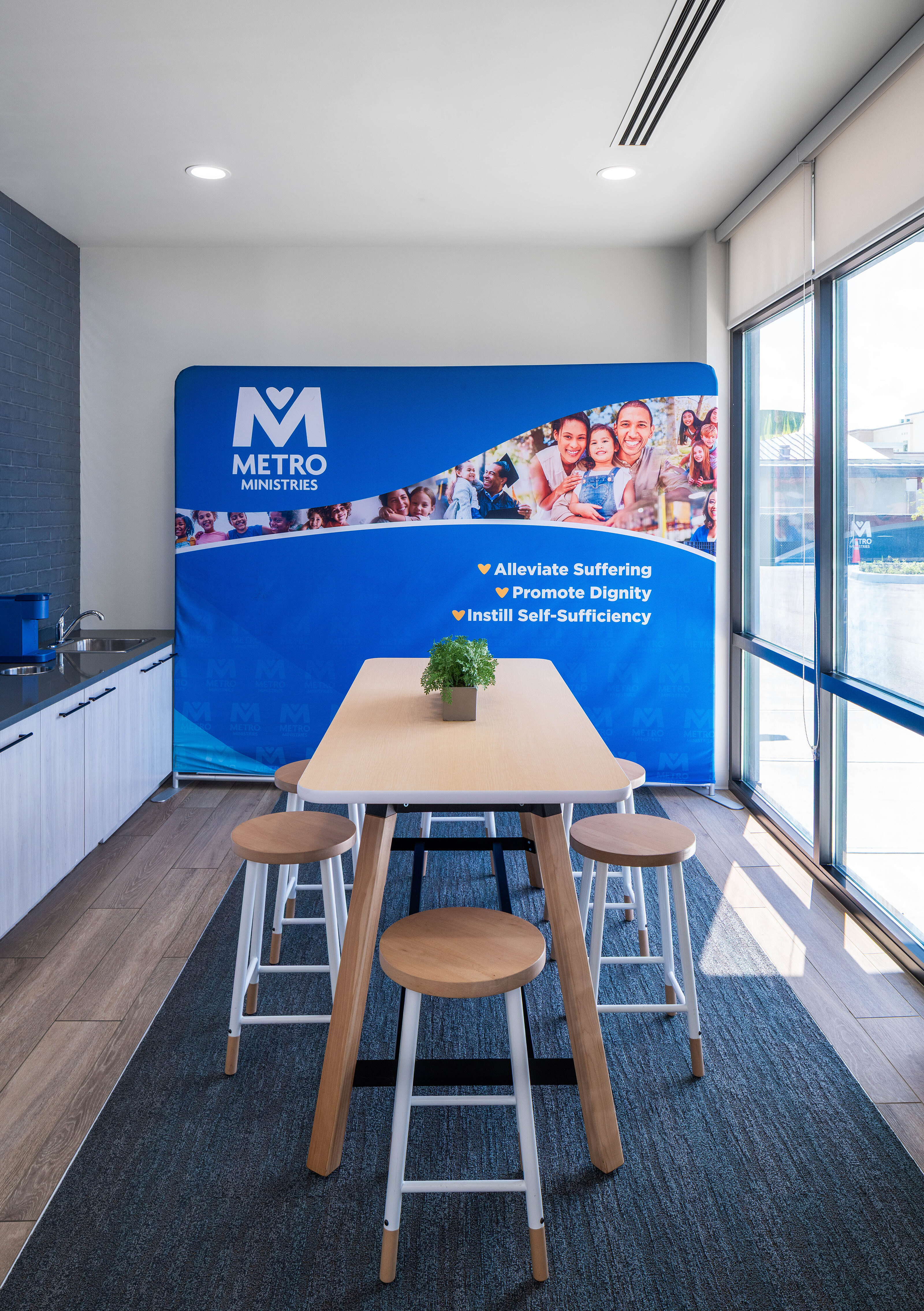 Break area with tall wood table, stools, cabinets, and a large Metro-branded display wall.