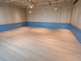 ADA-compliant multipurpose gathering room featuring light wood flooring, decorative blue wainscoting, paneled wood walls, and brass chandelier lighting.