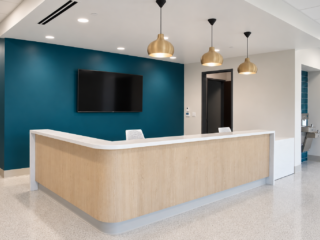 Reception desk with warm wood finishes, gold pendant lights and a teal accent wall.