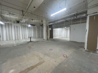 Unfinished open office interior with exposed utilities, partially finished walls and concrete flooring.