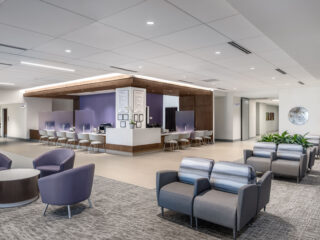 Clinical corridor with staff in scrubs and a workstation overlooking city buildings