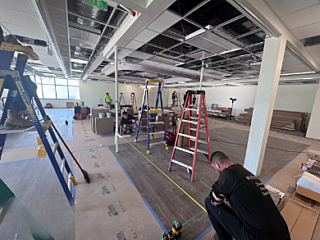 Construction site with open ceiling, ladders, workers, and materials throughout the workspace.