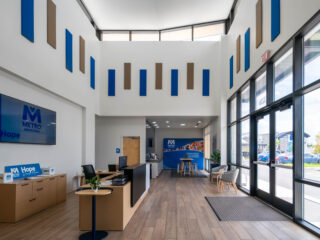 Modern lobby with wood floors, tall ceilings, and Metro-branded welcome desk near large windows.