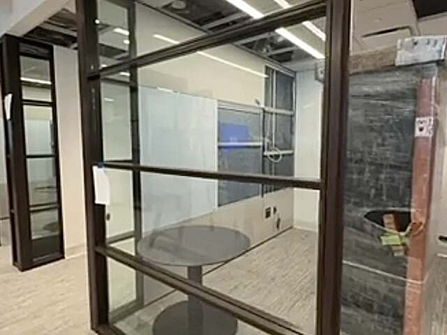 Glass-walled office under construction with exposed ceiling, table, and wrapped materials.