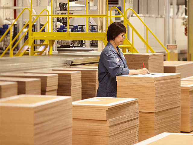 Worker inspecting stacked wood panels in a manufacturing facility.