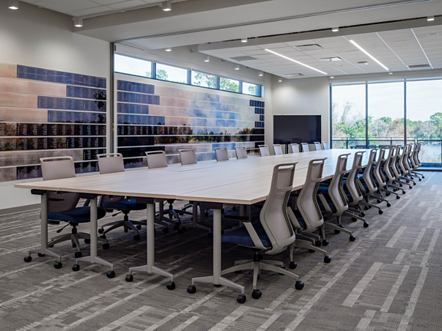 Large conference room with long table, ergonomic chairs, wall display, and floor-to-ceiling windows