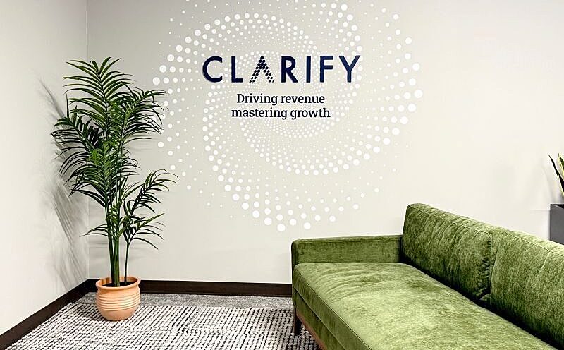Clarify reception area with a green sofa, potted plant and branded wall graphic.